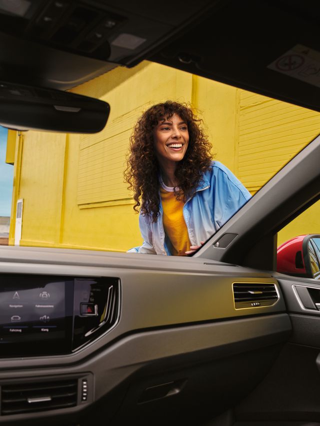 VW Taigo VW Taigo in Rot am Straßenrand vor gelbem Gebäude, Heck- und Seitenansicht, Frau geht auf Fahrzeug zu