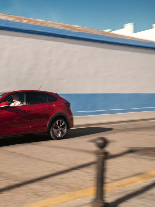 VW Taigo VW Taigo in Rot am Straßenrand vor gelbem Gebäude, Heck- und Seitenansicht, Frau geht auf Fahrzeug zu