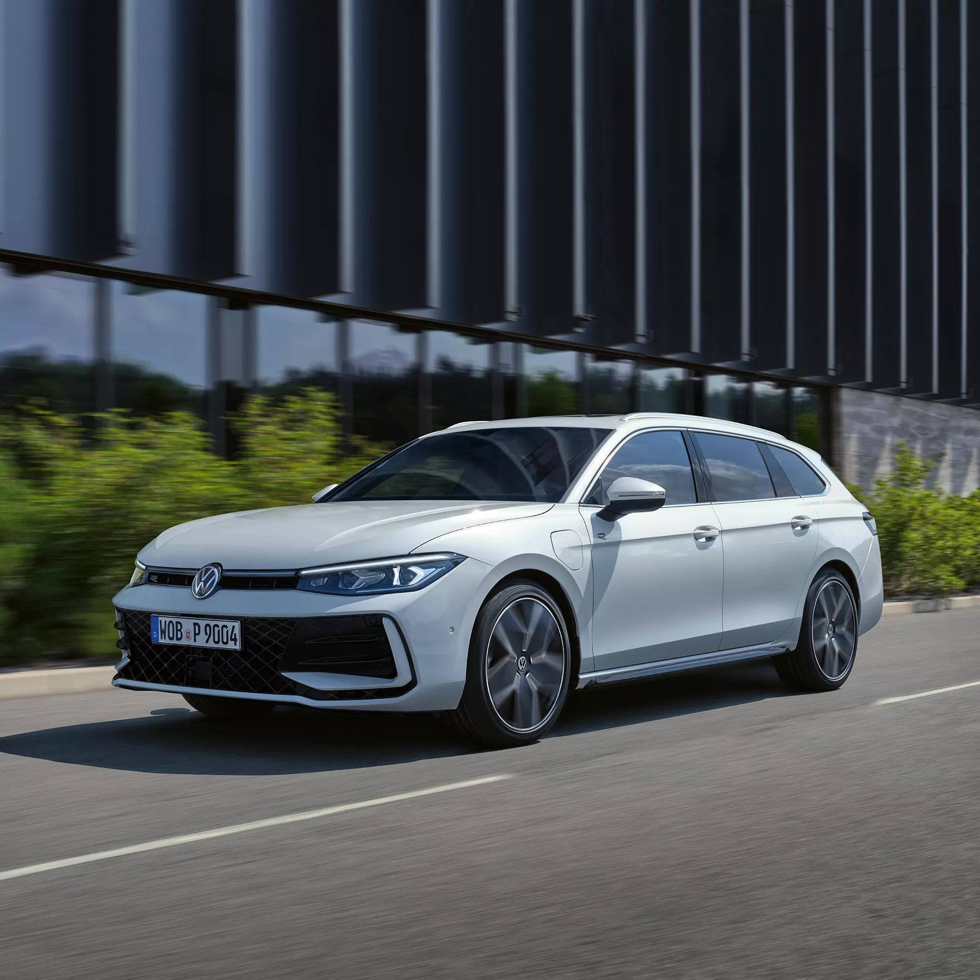 VW Der neue Passat VW Passat in weiß fährt seitlich an einem Gebäude vorbei.